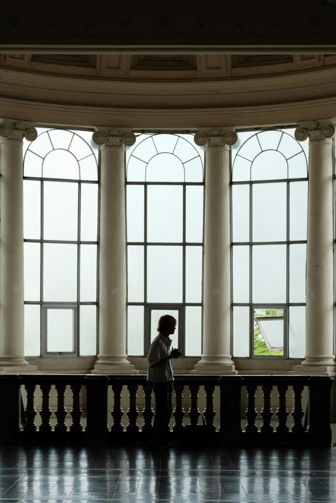 A lone person silhouetted against tall arched windows in a historic Ho Chi Minh City museum.